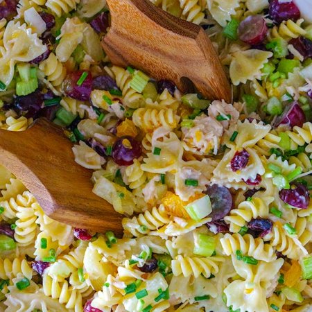 Pasta salad being picked up with salad servers.