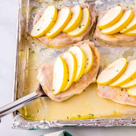 A pork chop being taken from a foil-lined baking sheet.