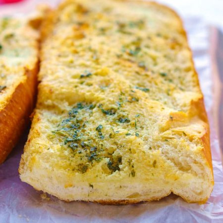 Baked garlic bread on a wooden cutting board.