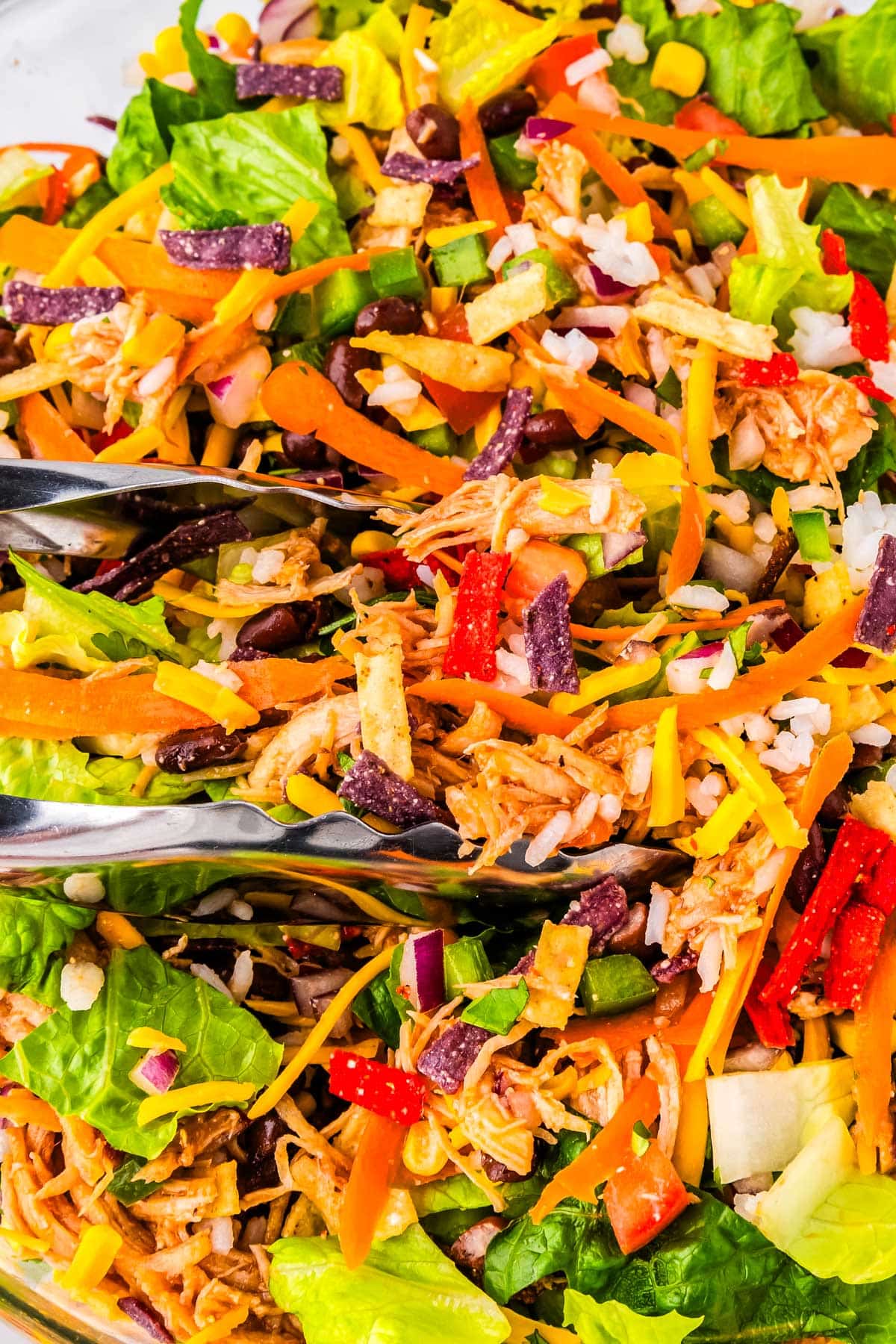 A close up picture of tongs in a BBQ Ranch Chicken Salad. 
