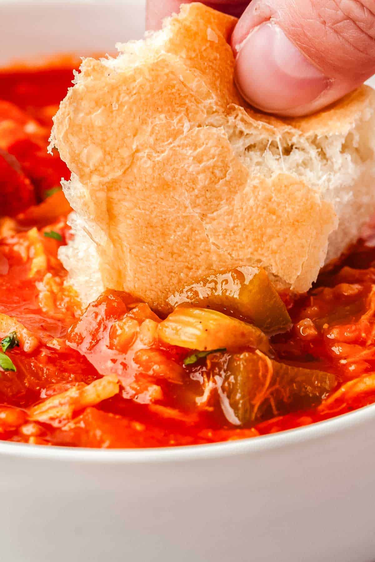 A piece of white dinner bread being dipped into a bowl of chicken sausage gumbo.