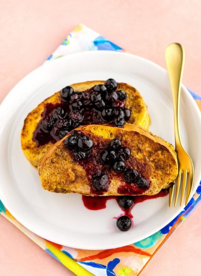 2 pieces of french toast on a while plate with blueberry sauce over the top of the toast.