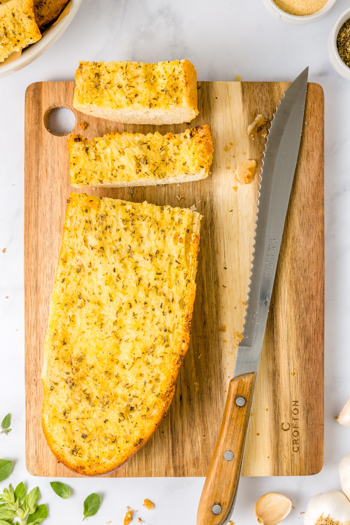 An overhead picture of Garlic Bread on a wooden cutting board with some slices cut off.