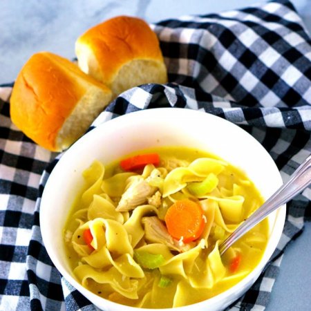Homemade chicken noodle soup in a white bowl served with rolls.