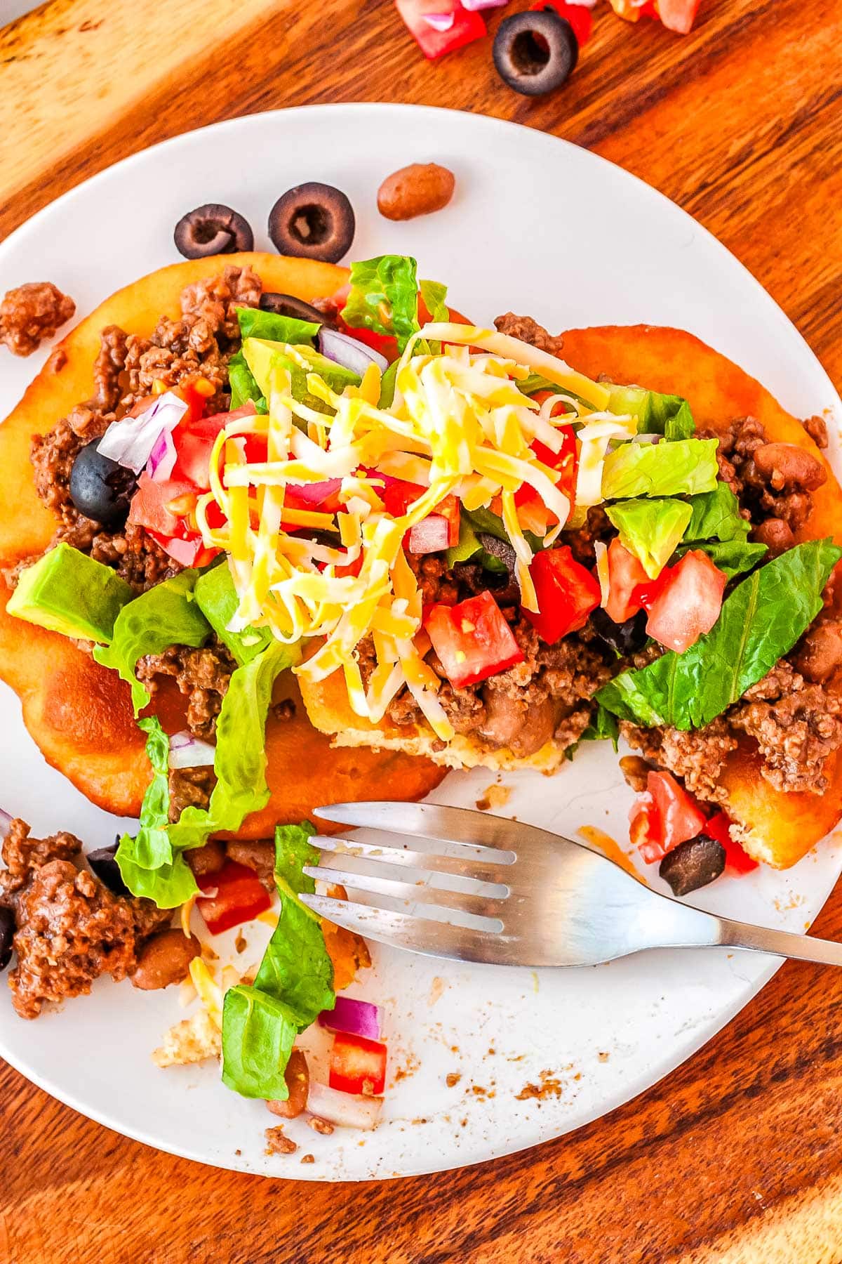 Two Fry bread tacos on a white plate with some forkfuls taken out of the food.