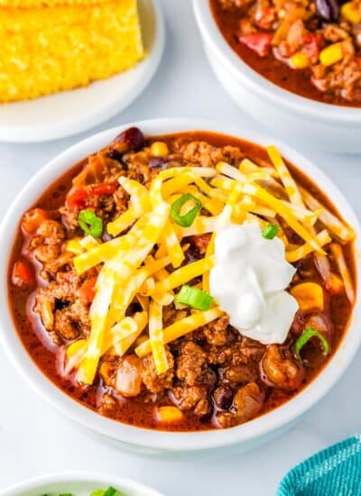 Chili in a white bowl with cornbread in the background.