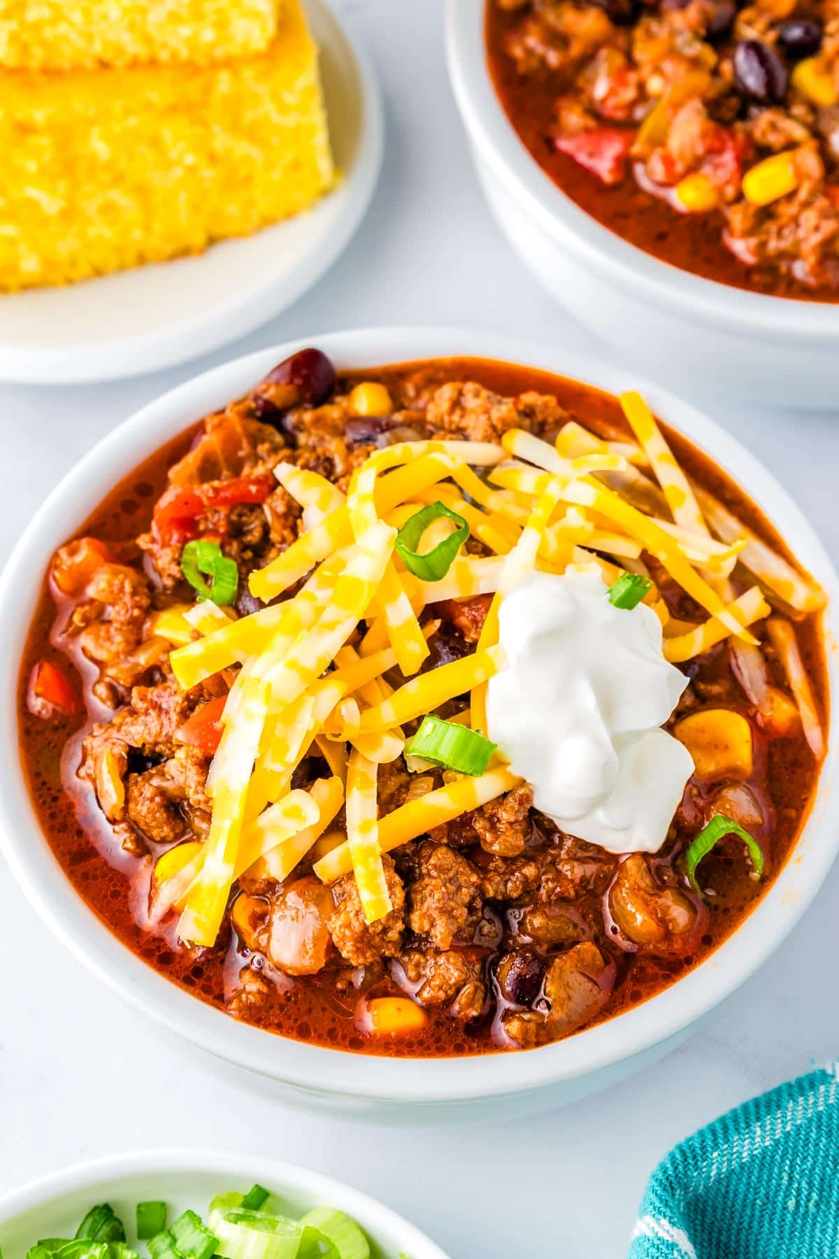 Chili in a white bowl with cornbread in the background. 