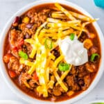 Chili With Corn in a white bowl garnished with cheese and sour cream.