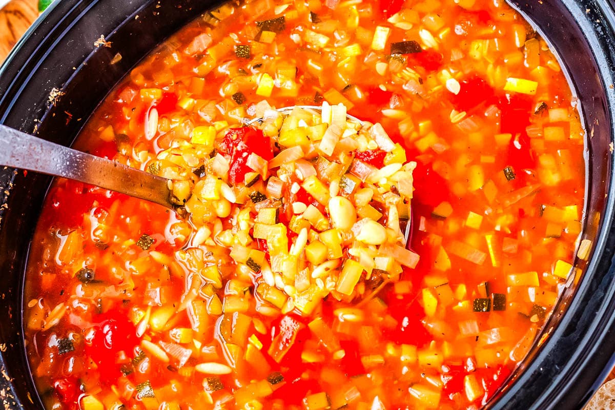 A ladeling picking up some Italian soup from a Crockpot.