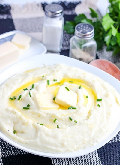Mashed Potatoes With Cream Cheese in a white serving bowl with pads of melted butter on top.
