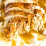 Close up image of slices of instant pot turkey breast on a bed of mashed potatoes and gravy.
