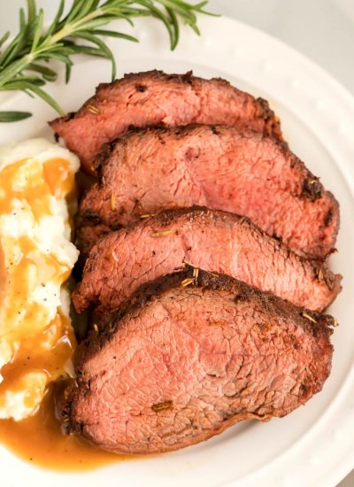 Beef roast on a plate with mashed potatoes and brown gravy.