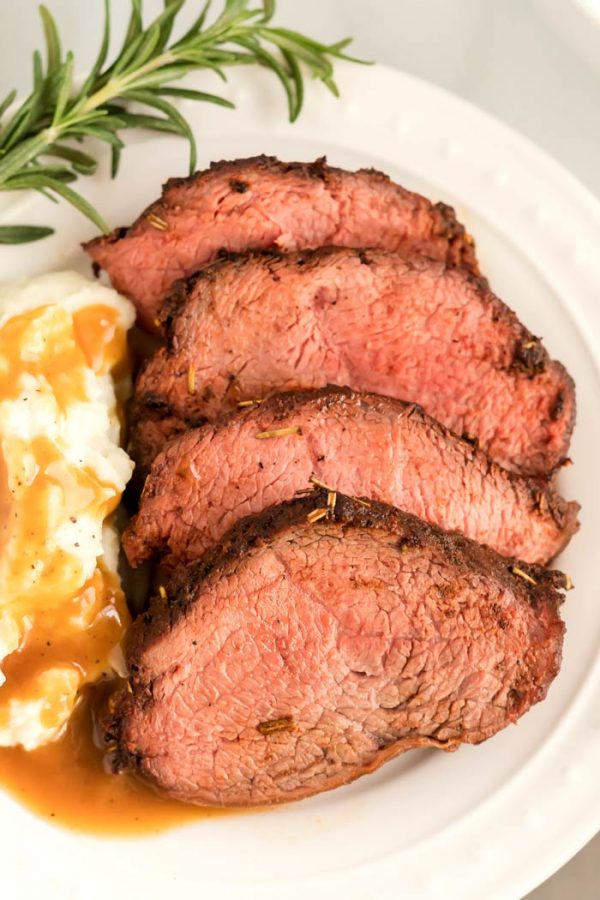Beef roast on a plate with mashed potatoes and brown gravy.