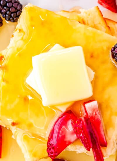 a stack of pancakes with butter, fruit and pancake syrup on top