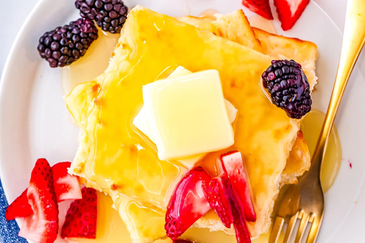 a stack of pancakes with syrup, butter, and fruit