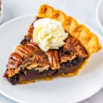 Chocolate pecan pie on a white dessert plate with a dollop of whipped cream.