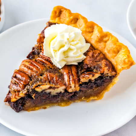 Chocolate pecan pie on a white dessert plate with a dollop of whipped cream.