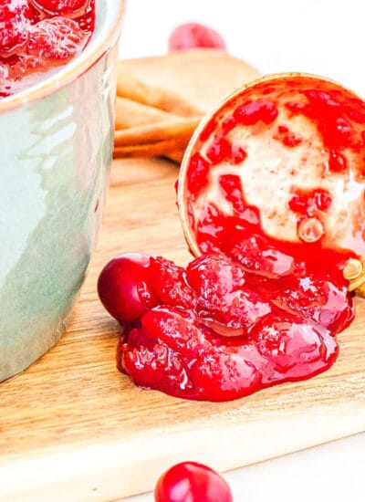 a ladle of cranberry sauce on a cutting board with a pot of cranberry sauce in the background