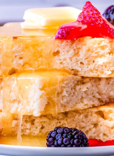 a stack of sheet pan pancakes on a plate with homemade pancake syrup and fruit