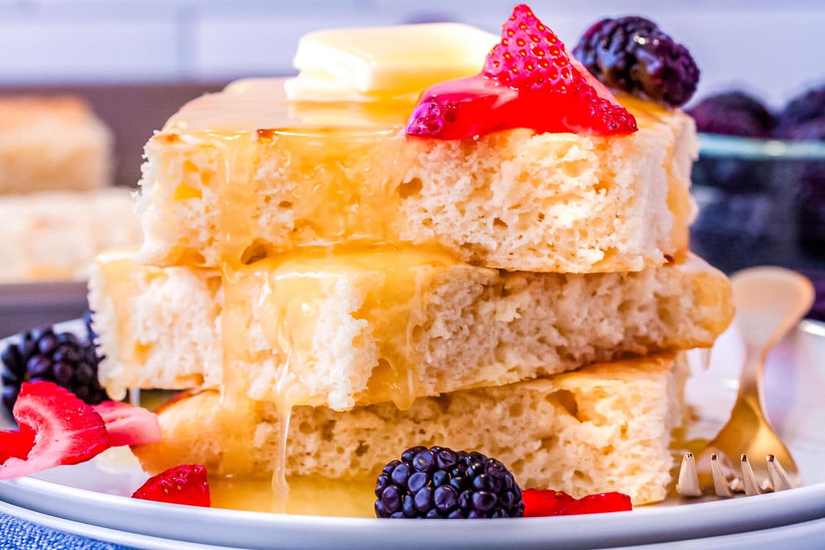 a stack of sheet pan pancakes on a plate with homemade pancake syrup and fruit