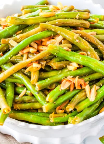 a white bowl of cooked green beans with slivered almonds