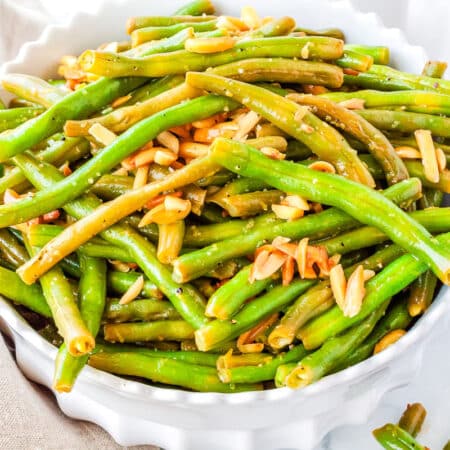 a white bowl of cooked green beans with slivered almonds