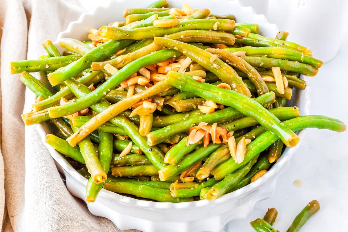 a white bowl of cooked green beans with slivered almonds