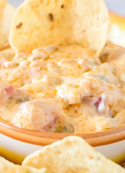 A close up picture of a bowl full of ROTEL Sausage Dip with a chip dipped into it.