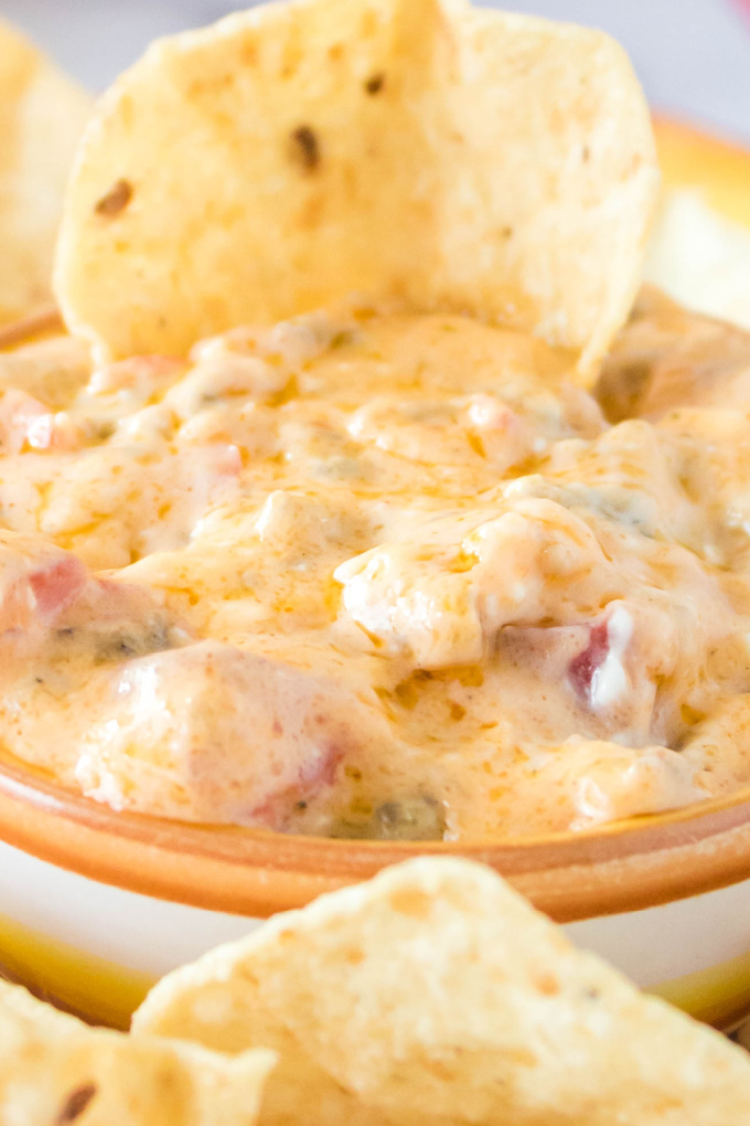 A close up picture of a bowl full of ROTEL Sausage Dip with a chip dipped into it.
