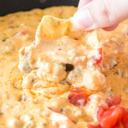 A chip dipping into the finished ROTEL Sausage Dip.
