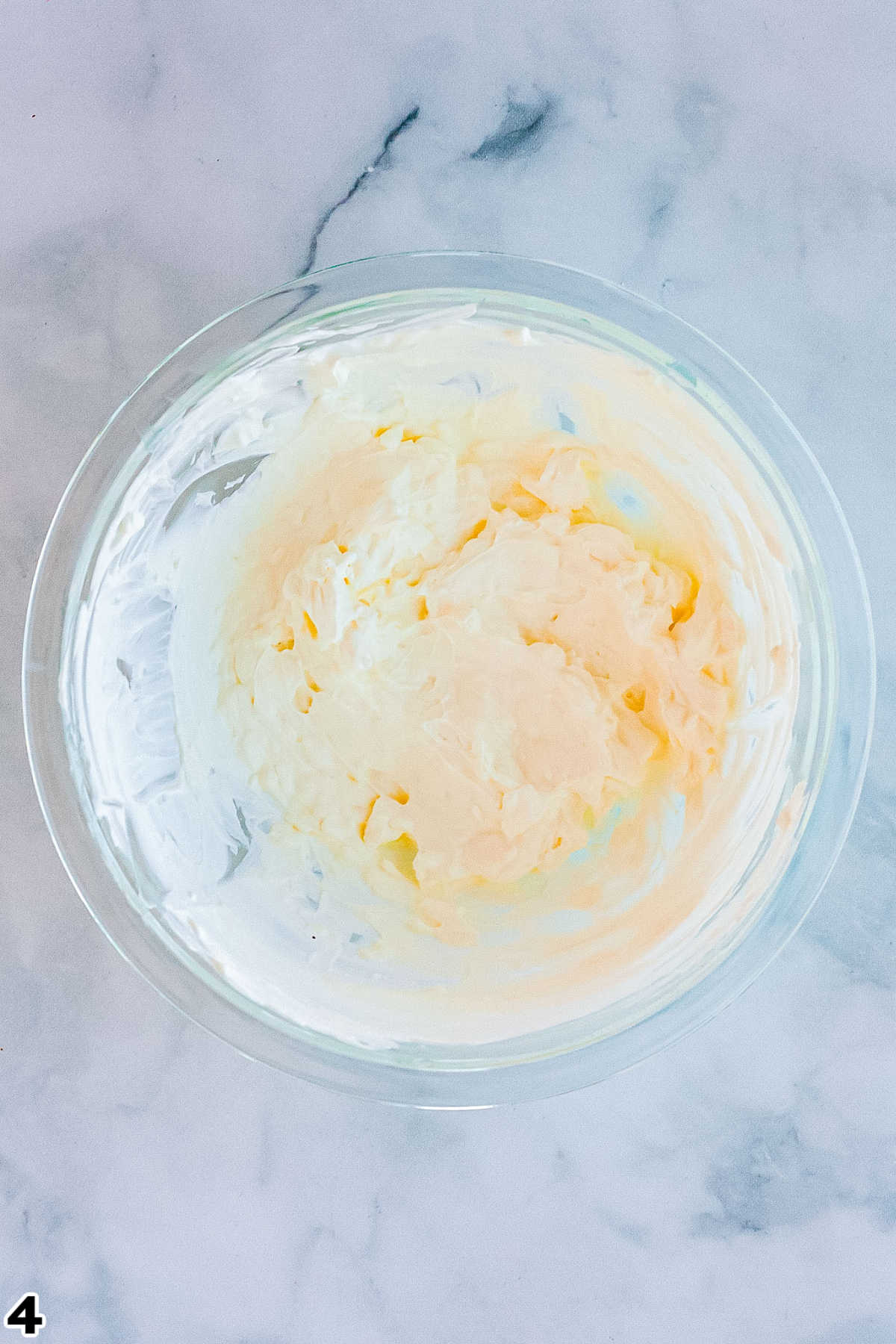 Sour cream and cream cheese beat together in a clear glass bowl.