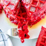 using a fork to take a bite of a stack of red velvet waffles on a plate