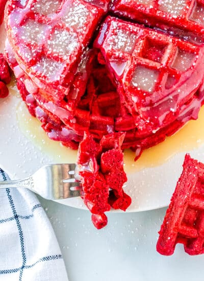 using a fork to take a bite of a stack of red velvet waffles on a plate