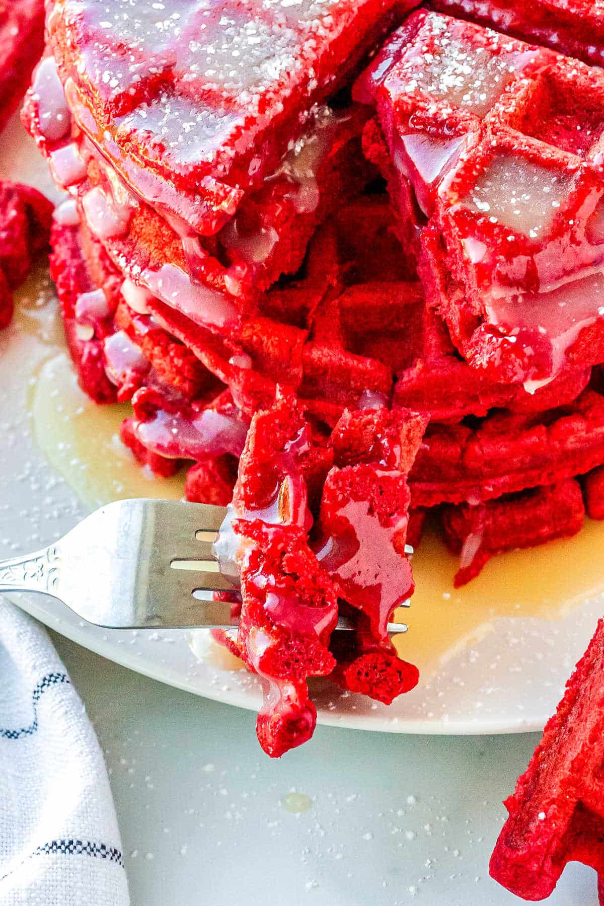 using a fork to take a bite of a stack of red velvet waffles on a plate