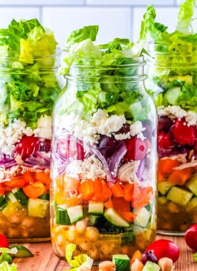 Three Mason Jar Greek Salads on a counter top.
