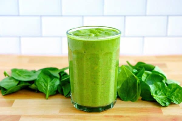 Green smoothie in a glass surrounded by Spinach.