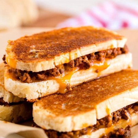 Grilled cheese sloppy joes stacked on a wooden cutting board.