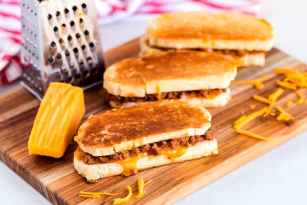 3 grilled cheese sandwiches on a wooden cutting board.