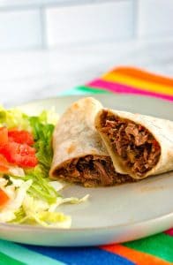 Machaca burrito cut in half on a white plate with shredded lettuce and chopped tomatoes.