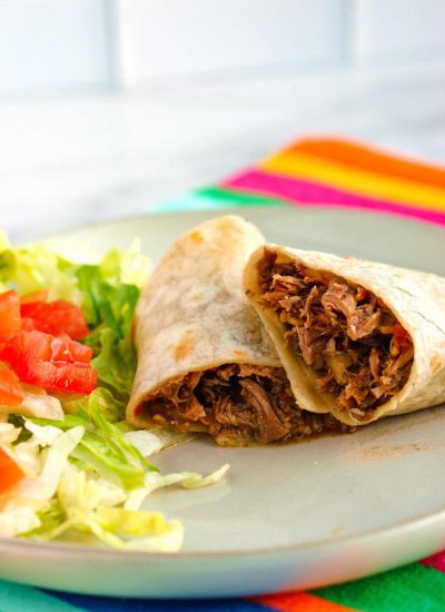 Machaca burrito cut in half on a white plate with shredded lettuce and chopped tomatoes.