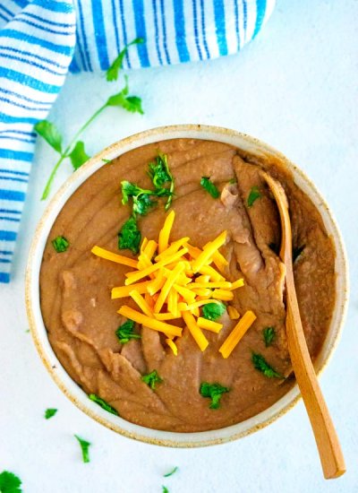 Instant Pot Refried Beans in a serving bowl garnished with cheese and cilantro.