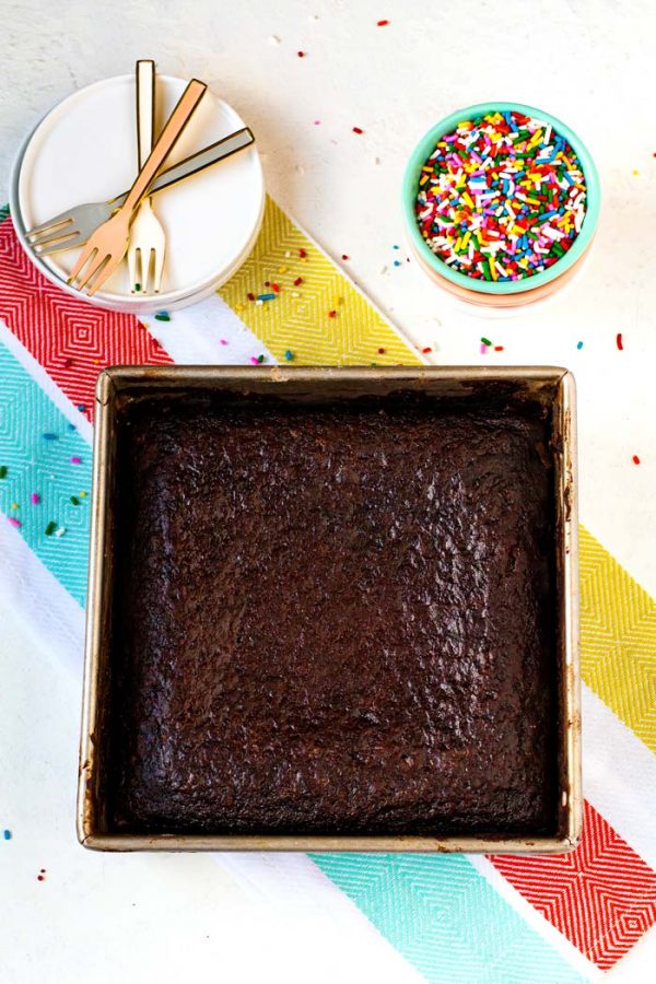 Overhead picture of a Chocolate Wacky Cake surrounded by sprinkles, white plates, and forks. 