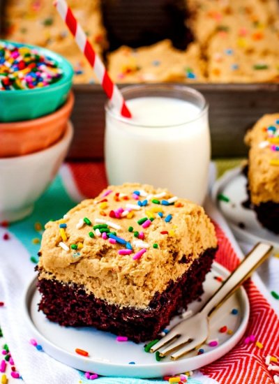 A slice cod chocolate wacky cake with peanut butter frosting that's topped with rainbow sprinkles on a white plate.