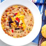 A white bowl full of crock pot white chicken chili with corn muffins.