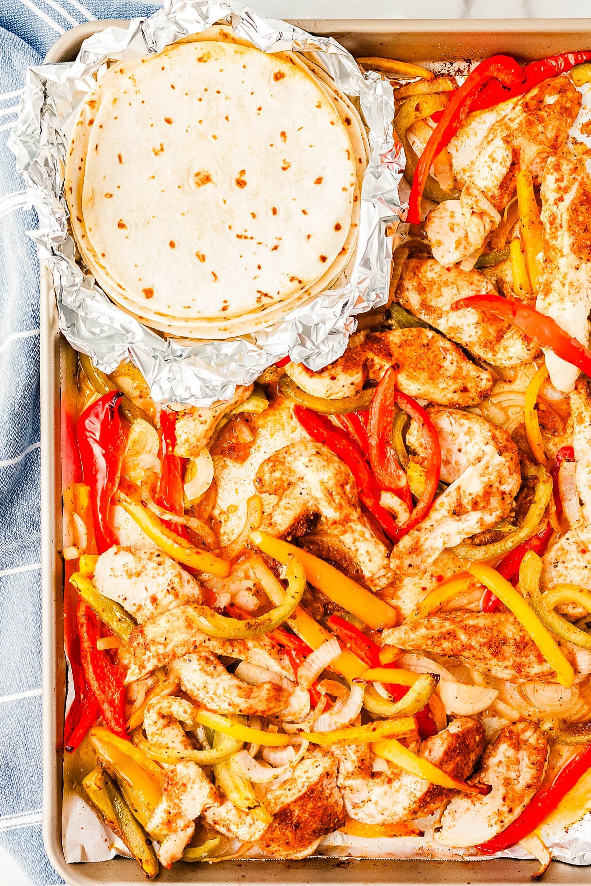 The finished Sheet Pan Fajitas on a sheet pan along with tortillas.