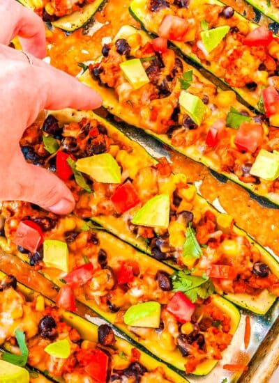 A hand picking up one of the finished Zucchini Taco Boats from a baking sheet.