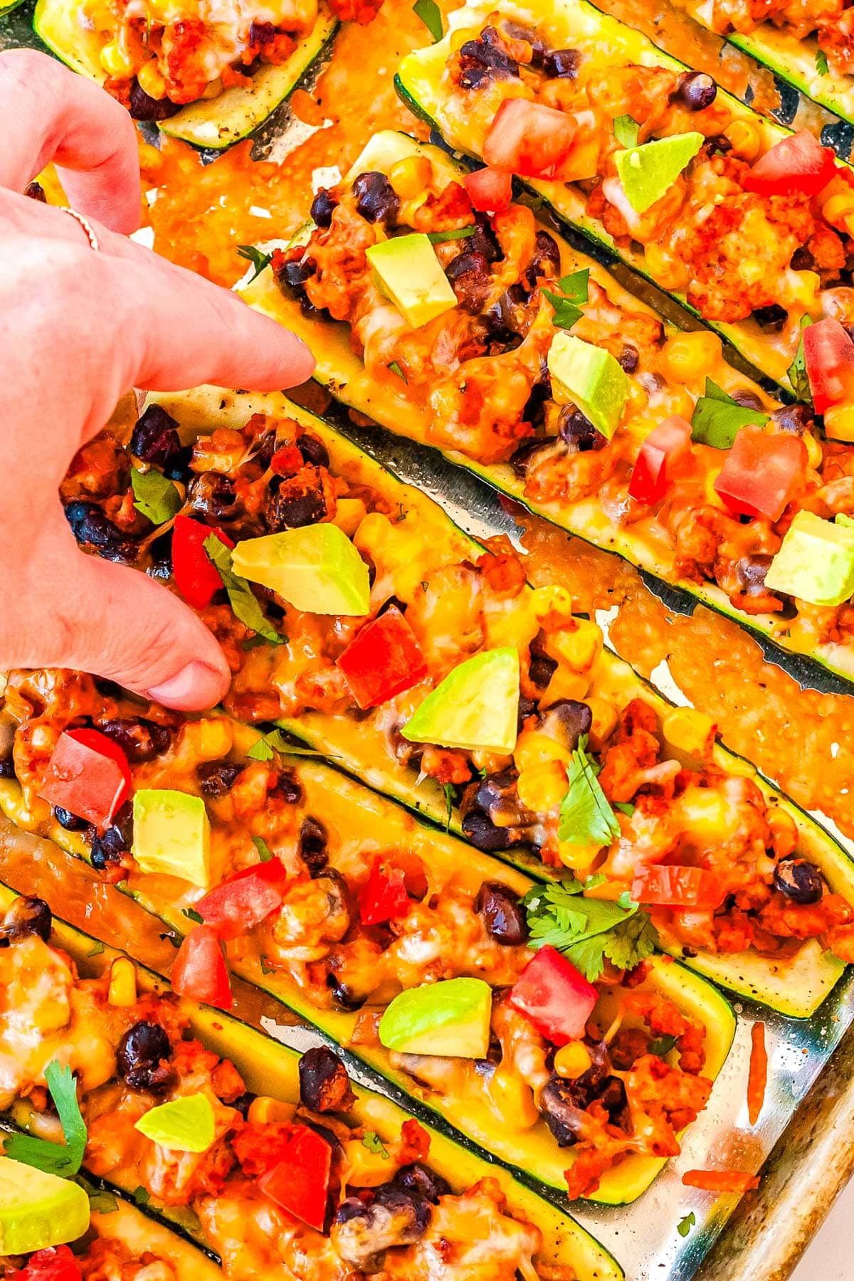 A hand picking up one of the finished Zucchini Taco Boats from a baking sheet.