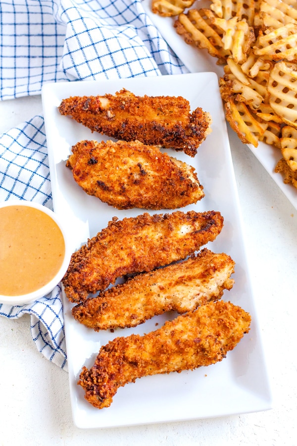 Overhead picture of homemade chicken fingers on a platter with a small bowl of dipping sauce.