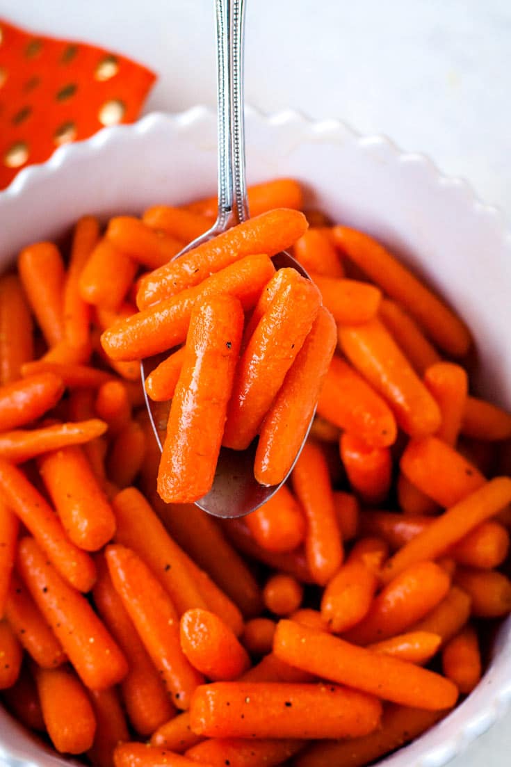 An overhead picture of brown sugar glazed carrots with a serving spoon scooping up some of the carrots.
