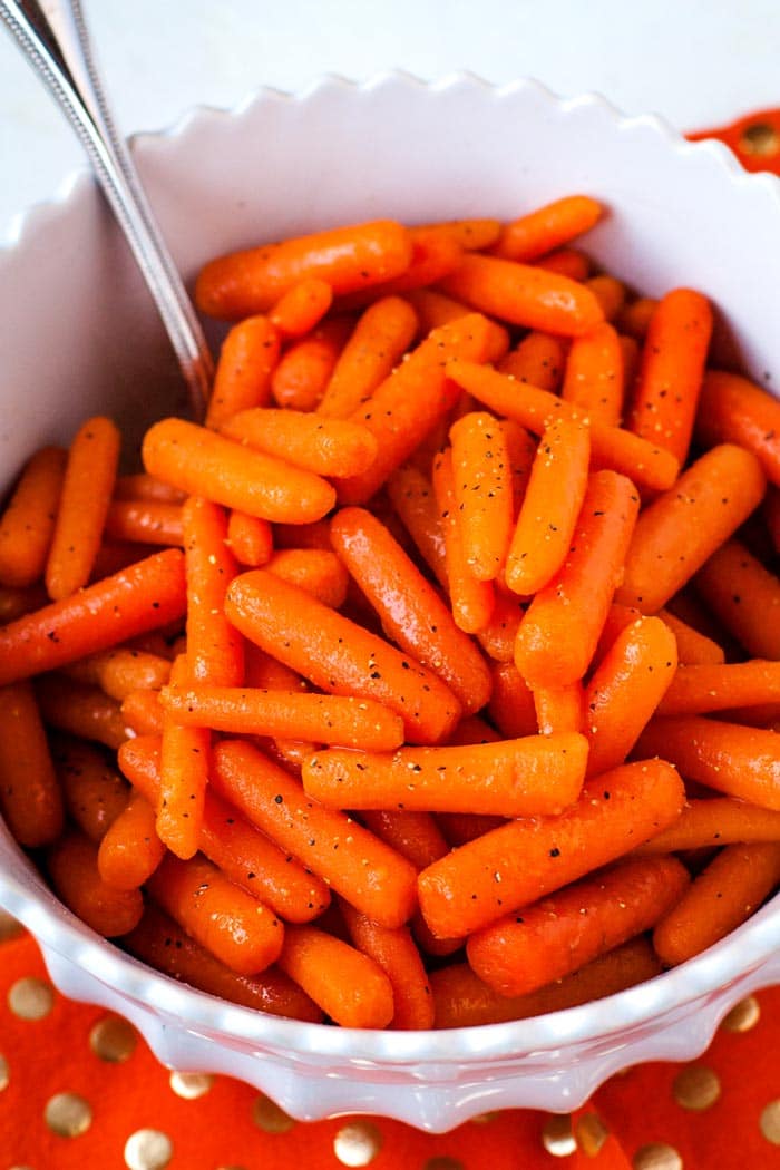 Finished glazed carrots in a white serving bowl with a serving spoon.